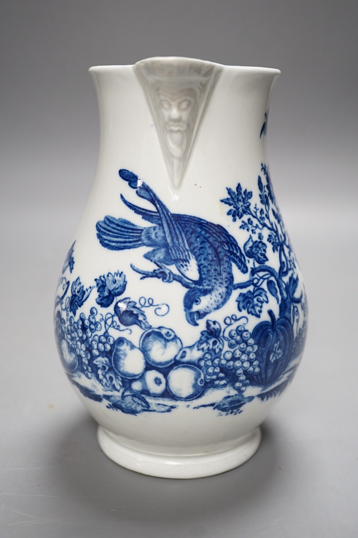 A Caughley baluster mask jug printed in underglaze blue with the 'parrot pecking fruit', 18.5cms high